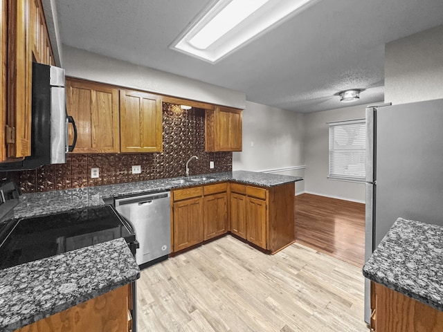 539 Mel Ct, Euless, TX 76039 - kitchen featuring appliances with stainless steel finishes, a sink, brown cabinets, light wood-type flooring, and a textured ceiling