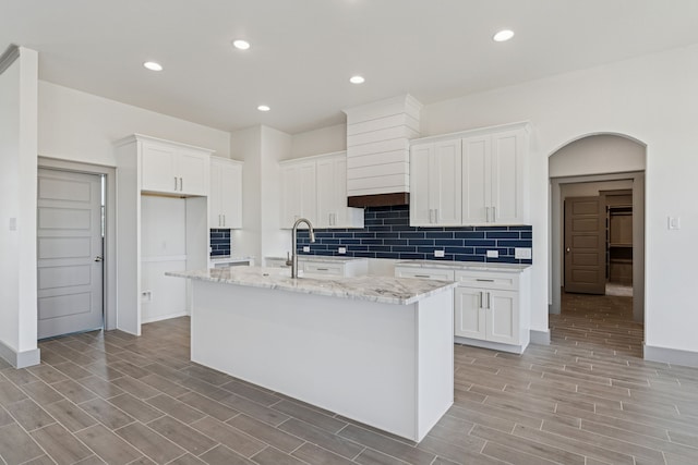 106 Maverick Way, Boyd, TX 76023 - kitchen featuring a center island with sink, decorative backsplash, wood tiled floors, white cabinets, and light stone countertops