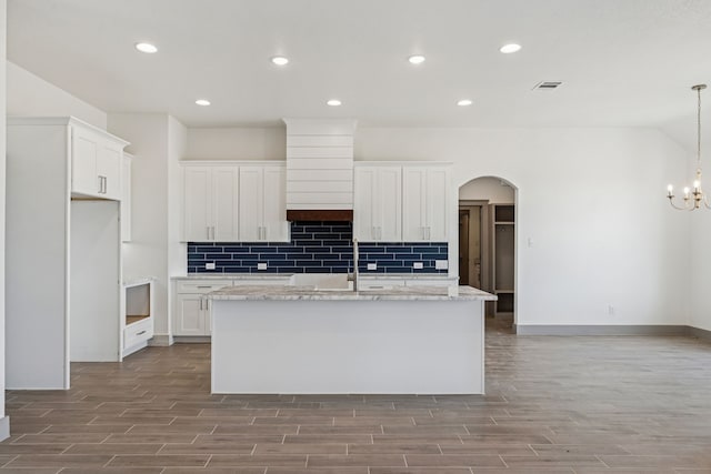 106 Maverick Way, Boyd, TX 76023 - kitchen with arched walkways, wood finished floors, an island with sink, decorative backsplash, and white cabinets