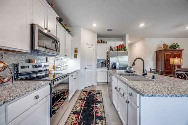 525 Brandy Ln, Tom Bean, TX 75489 - kitchen featuring appliances with stainless steel finishes, a sink, light wood-style flooring, an island with sink, and white cabinets