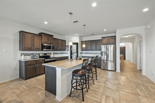 11512 Starlight Ranch Trl, Fort Worth, TX 76052 - kitchen with appliances with stainless steel finishes, tasteful backsplash, arched walkways, dark brown cabinets, and a breakfast bar