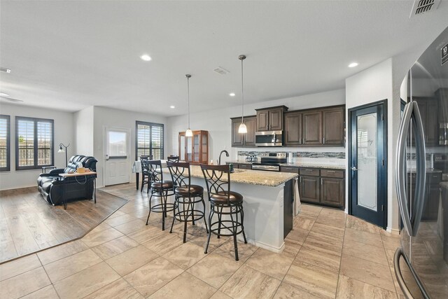 11512 Starlight Ranch Trl, Fort Worth, TX 76052 - kitchen with appliances with stainless steel finishes, dark brown cabinets, open floor plan, a kitchen breakfast bar, and light stone counters