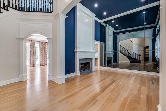 805 Cross Ln, Southlake, TX 76092 - unfurnished living room featuring decorative columns, a premium fireplace, light wood-type flooring, stairs, and a high ceiling