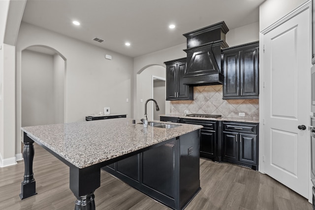 7913 Heritage Palms Trl, Mckinney, TX 75070 - kitchen featuring a sink, arched walkways, dark cabinets, stainless steel gas stovetop, and a center island with sink