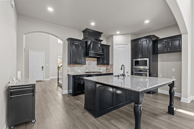 7913 Heritage Palms Trl, Mckinney, TX 75070 - kitchen with appliances with stainless steel finishes, dark cabinetry, a sink, arched walkways, and decorative backsplash