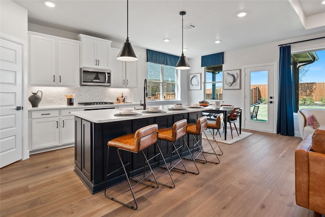 3105 Patrinia St, Royse City, TX 75189 - kitchen with stainless steel microwave, light countertops, a kitchen island with sink, white cabinetry, and light wood-type flooring
