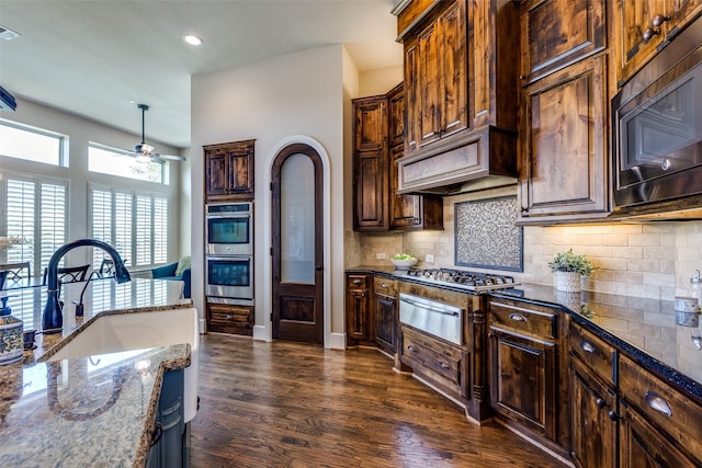 4540 Honeyvine Ln, Prosper, TX 75078 - kitchen featuring stainless steel appliances, a warming drawer, ceiling fan, dark stone counters, and dark wood-style floors
