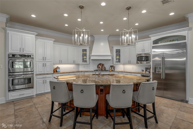 609 Enchanted Ln, Bossier City, LA 71111 - kitchen with built in appliances, ornamental molding, a center island with sink, a chandelier, and premium range hood