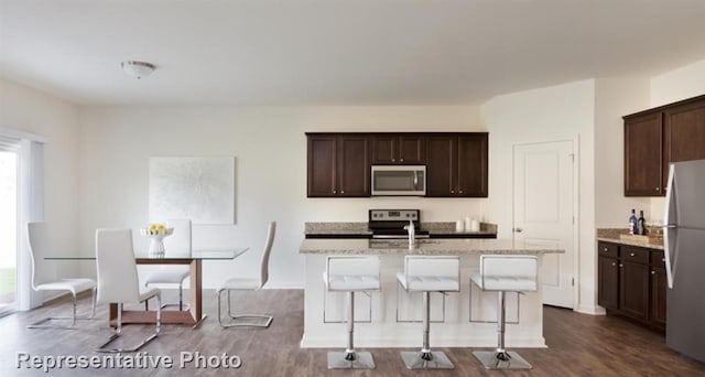 4924 Mccoy, Fort Worth, TX 76179 - kitchen featuring appliances with stainless steel finishes, dark wood-style floors, dark brown cabinets, a breakfast bar area, and light stone counters