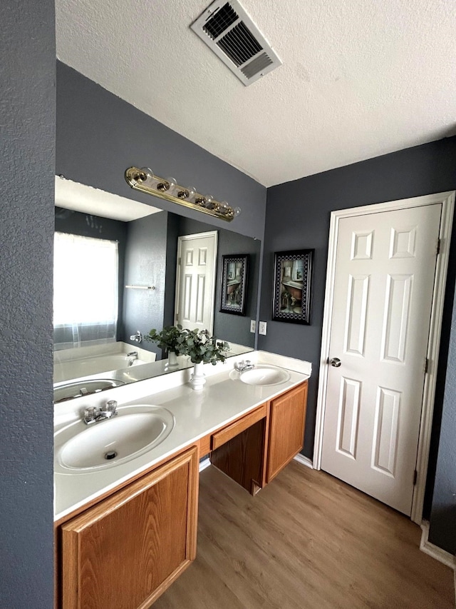 1505 Yellowbird Ct, Desoto, TX 75115 - bathroom featuring wood finished floors, double vanity, a bath, and a textured ceiling