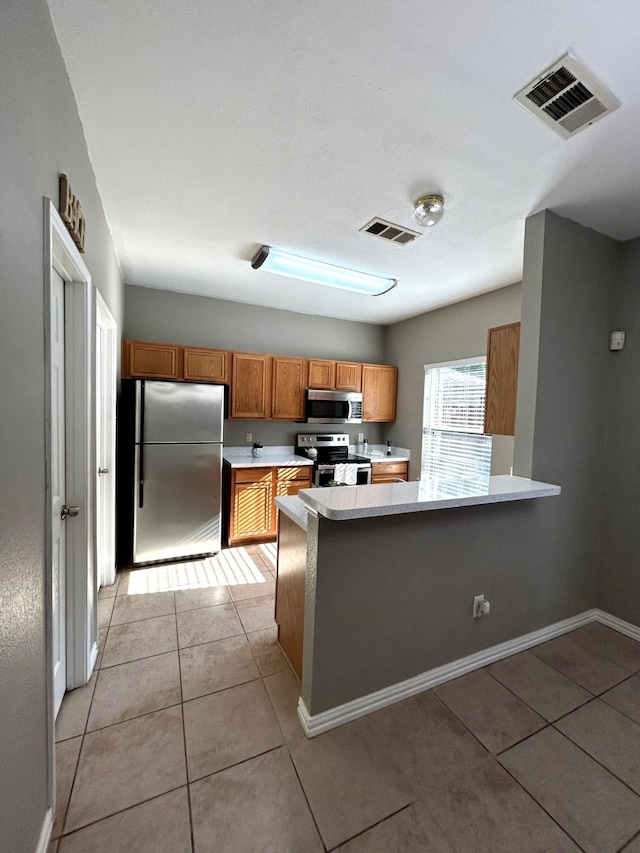 1505 Yellowbird Ct, Desoto, TX 75115 - kitchen with stainless steel appliances, light countertops, brown cabinets, a peninsula, and light tile patterned floors