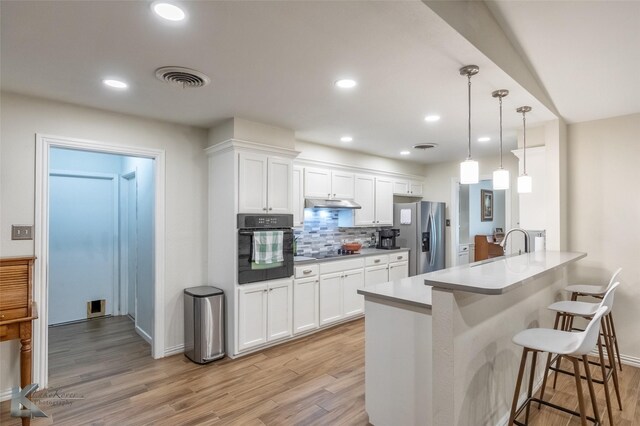 3126 Salinas Dr, Abilene, TX 79605 - kitchen featuring black appliances, a kitchen bar, a peninsula, light wood-style flooring, and decorative backsplash