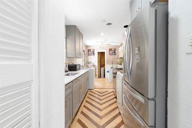 11103 Tascosa St, Dallas, TX 75228 - kitchen featuring gray cabinets, washer / dryer, freestanding refrigerator, light countertops, and brick wall