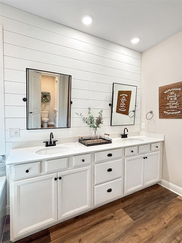2219 Wellington Ln, Corinth, TX 76210 - bathroom featuring double vanity, toilet, wood finished floors, baseboards, and wood walls