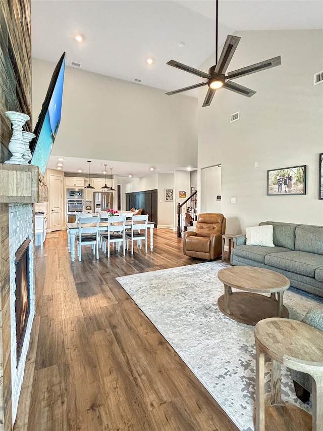 2219 Wellington Ln, Corinth, TX 76210 - living area with a high ceiling, a glass covered fireplace, dark wood-style floors, a ceiling fan, and stairs