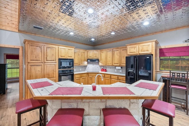 108 Fcr 868, Teague, TX 75860 - kitchen with black appliances, tile counters, light wood-style floors, tasteful backsplash, and a kitchen breakfast bar