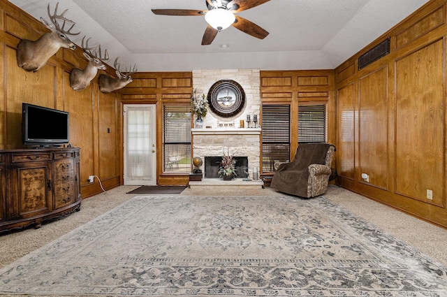 3313 Conlin Dr, Rowlett, TX 75088 - carpeted living area featuring ceiling fan, wooden walls, a stone fireplace, and a textured ceiling