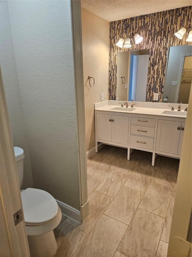 864 Fairview Dr, Krugerville, TX 76227 - full bathroom featuring baseboards, double vanity, toilet, a textured wall, and a textured ceiling