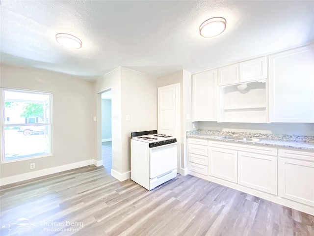 2234 Meander St, Abilene, TX 79602 - kitchen with white gas range, light wood-type flooring, white cabinets, a textured ceiling, and baseboards