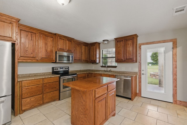 2790 Fairview Rd, Millsap, TX 76066 - kitchen with stainless steel appliances, a kitchen island, brown cabinets, a sink, and light tile patterned floors