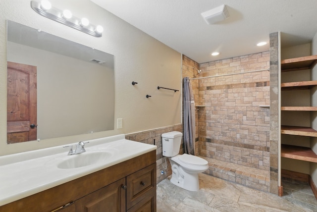 2790 Fairview Rd, Millsap, TX 76066 - bathroom featuring vanity, a tile shower, toilet, tile walls, and wainscoting