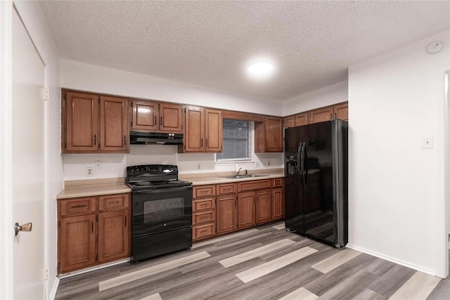 1030 Tyler St, Cooper, TX 75432 - kitchen featuring black appliances, under cabinet range hood, light countertops, a sink, and light wood finished floors
