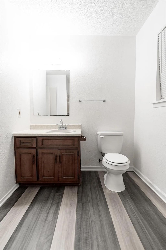 1030 Tyler St, Cooper, TX 75432 - bathroom featuring wood finished floors, toilet, vanity, baseboards, and a textured ceiling