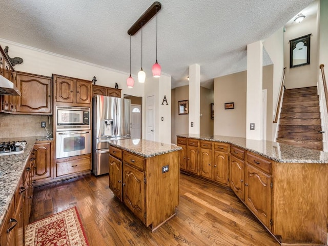 3968 Valez Dr, Carrollton, TX 75007 - kitchen featuring appliances with stainless steel finishes, a kitchen island, a textured ceiling, dark wood finished floors, and light stone counters