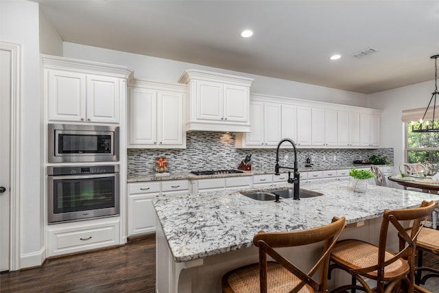321 Hitch Wagon Dr, Mckinney, TX 75071 - kitchen featuring appliances with stainless steel finishes, a sink, decorative backsplash, dark wood finished floors, and a center island with sink