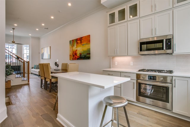 4651 New Water Ln, Dallas, TX 75219 - kitchen featuring stainless steel appliances, ornamental molding, a breakfast bar area, light wood finished floors, and light countertops