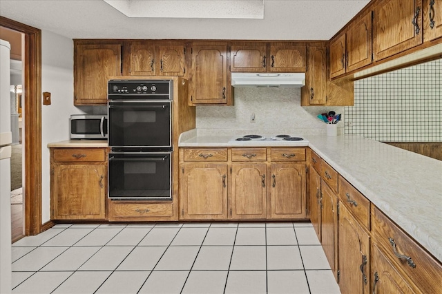 3601 University Dr, Garland, TX 75043 - kitchen with stainless steel microwave, under cabinet range hood, light countertops, white electric stovetop, and brown cabinets