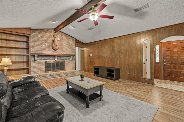 3601 University Dr, Garland, TX 75043 - living room featuring a textured ceiling, a ceiling fan, wood walls, wood finished floors, and a fireplace