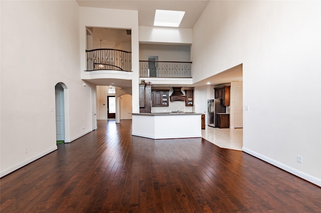 1101 Anchor Ter, Irving, TX 75063 - unfurnished living room with arched walkways, dark wood-type flooring, a towering ceiling, a skylight, and baseboards