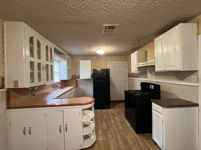 3304 Fadal Ave, Waco, TX 76708 - kitchen featuring black appliances, under cabinet range hood, a peninsula, white cabinetry, and light wood-style floors