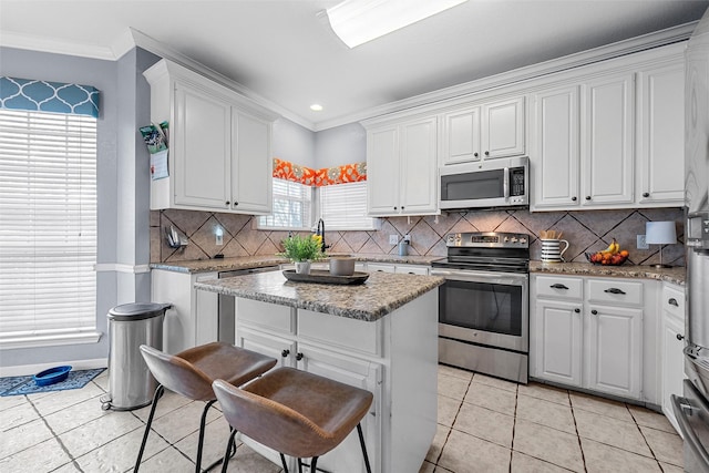 209 Keswick Dr, Hewitt, TX 76643 - kitchen featuring stainless steel appliances, white cabinets, a kitchen island, light tile patterned floors, and ornamental molding