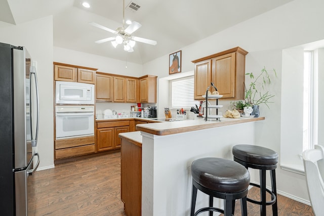 1415 Clubhill Dr, Rockwall, TX 75087 - kitchen featuring white appliances, a peninsula, vaulted ceiling, a kitchen breakfast bar, and dark wood-style floors