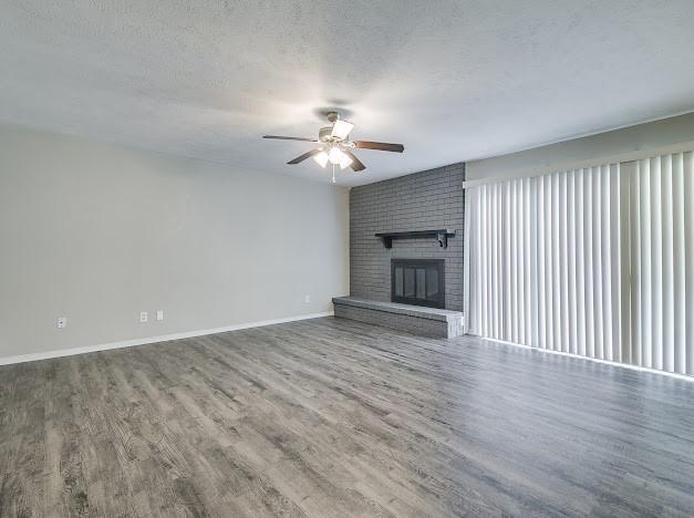 1901 Castille Dr, Carrollton, TX 75007 - unfurnished living room with ceiling fan, wood finished floors, baseboards, a brick fireplace, and a textured ceiling