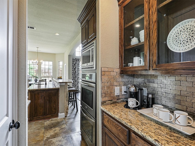 2420 Lilyfield Dr, Trophy Club, TX 76262 - kitchen featuring stainless steel appliances, light stone countertops, glass insert cabinets, backsplash, and a chandelier
