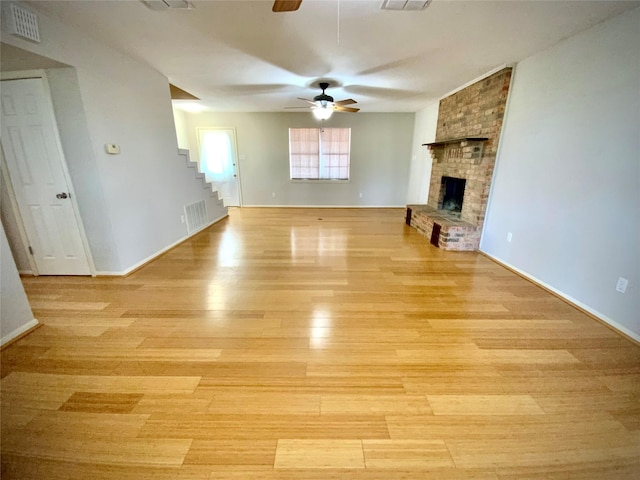 1409 W Trinity, Groesbeck, TX 76642 - unfurnished living room with a ceiling fan, stairway, light wood-style flooring, a brick fireplace, and baseboards