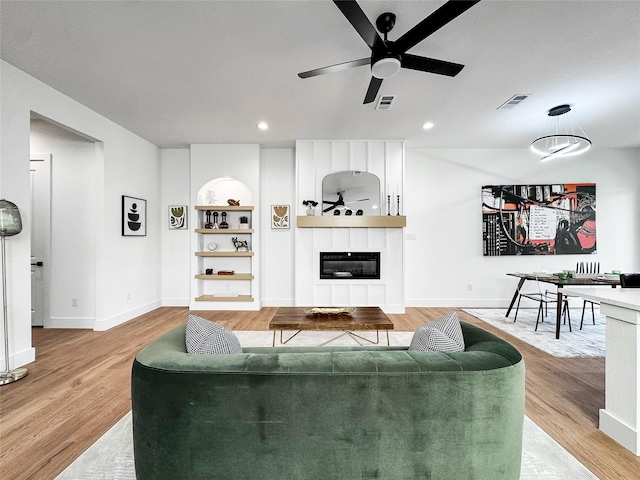 2417 Merlin St, Dallas, TX 75215 - living room featuring a ceiling fan, a fireplace, baseboards, built in shelves, and light wood finished floors