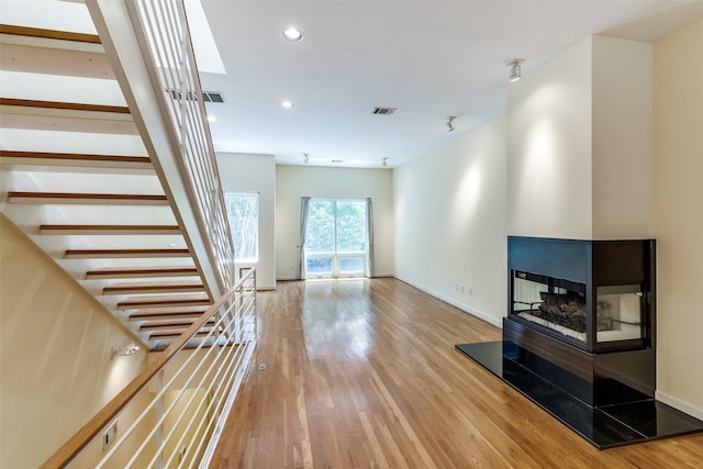 4100 Travis St Unit 19, Dallas, TX 75204 - unfurnished living room featuring wood finished floors, recessed lighting, stairs, a multi sided fireplace, and baseboards