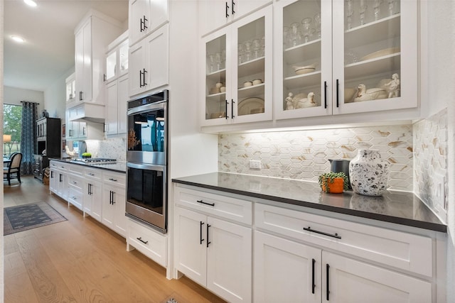1804 Rockwood Ln, Mansfield, TX 76063 - kitchen with stainless steel appliances, dark countertops, light wood-style flooring, backsplash, and white cabinetry