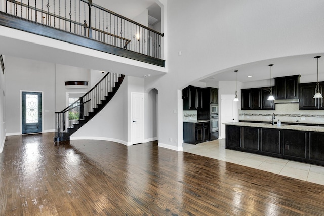 1708 Stillwater Dr, Burleson, TX 76028 - unfurnished living room featuring a high ceiling, light wood finished floors, baseboards, stairs, and arched walkways