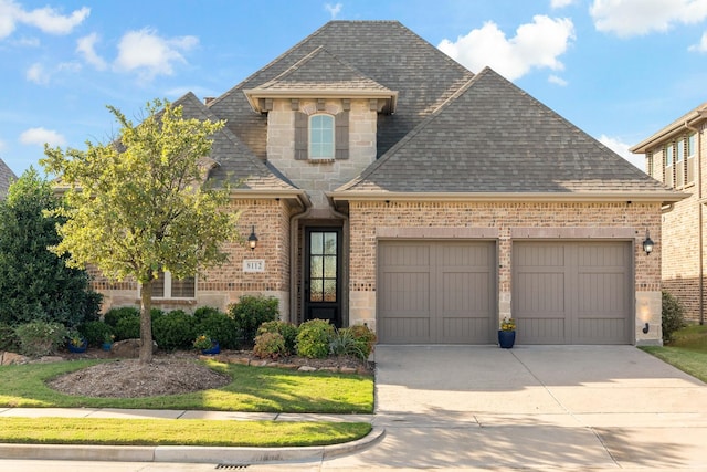8112 Western, The Colony, TX 75056 - french country home with roof with shingles, a garage, concrete driveway, and brick siding