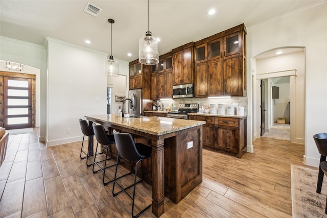 1308 Green Ridge Rd, Weatherford, TX 76085 - kitchen featuring stainless steel appliances, ornamental molding, a kitchen bar, a kitchen island with sink, and light wood finished floors