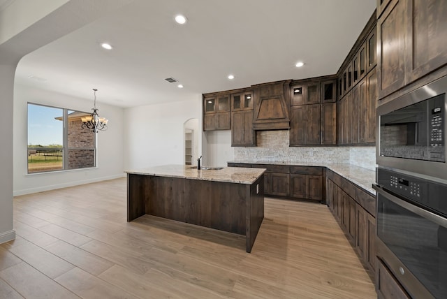 411 Solo Ridge Dr, Waxahachie, TX 75167 - kitchen featuring stainless steel oven, arched walkways, tasteful backsplash, built in microwave, and a chandelier