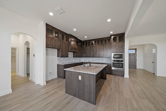 411 Solo Ridge Dr, Waxahachie, TX 75167 - kitchen with stainless steel oven, built in microwave, dark brown cabinets, arched walkways, and decorative backsplash