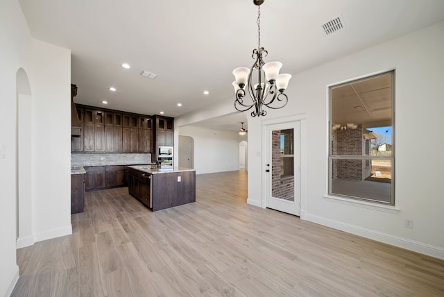 411 Solo Ridge Dr, Waxahachie, TX 75167 - kitchen featuring arched walkways, dark brown cabinets, a center island with sink, stainless steel microwave, and backsplash