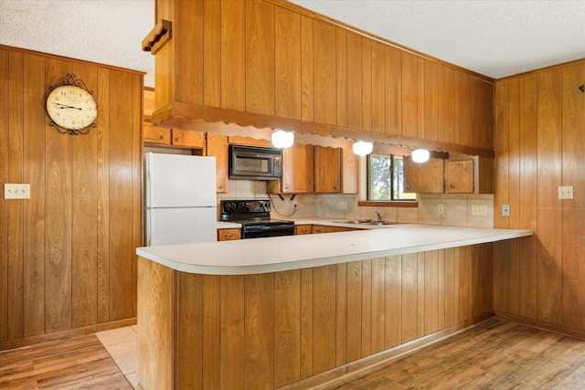 1023 Holmes Dr, Granbury, TX 76048 - kitchen featuring black appliances, brown cabinetry, wooden walls, light wood-type flooring, and light countertops