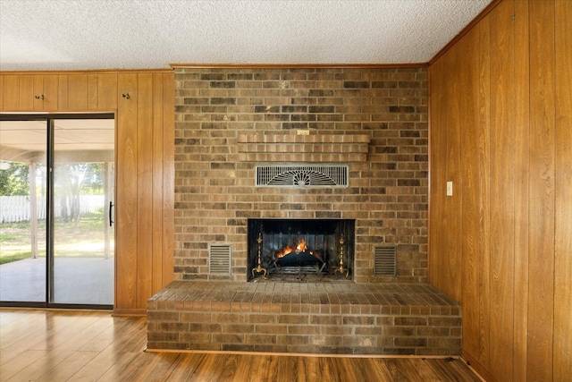 1023 Holmes Dr, Granbury, TX 76048 - unfurnished living room with wooden walls, a textured ceiling, wood finished floors, ornamental molding, and a brick fireplace